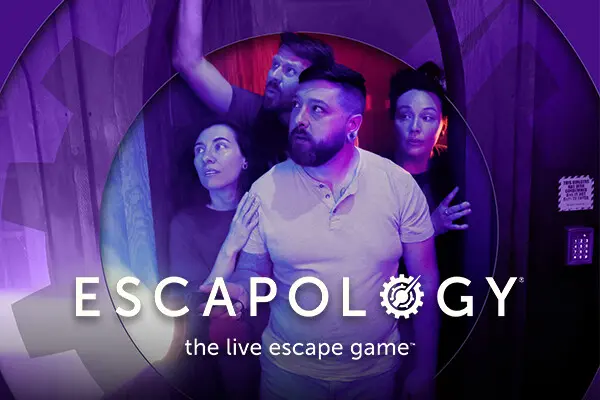 Group posing with excitement inside Escapology escape room under purple lighting.